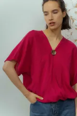 Blusa de lino color fucsia, con escote en V y manga corta amplia. Presenta un detalle de botón decorativo dorado en el centro del escote.
