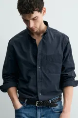 Camisa de corte regular fit confeccionada en tejido de algodón. Presenta cuello con solapa abotonada, cierre frontal con botones, manga larga con puños abotonados y un bolsillo plastrón en el pecho.