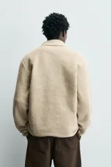 Sudadera de corte relajado confeccionada en tejido con textura, color beige. Presenta cuello solapa con cierre frontal de cremallera, manga larga y acabados con cinta elástica en puños y ruedo.