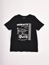 Remera negra de manga corta con cuello redondo y un estampado frontal en blanco que conmemora el Gran Premio Automovilístico de Mónaco de 1957, con un coche de carreras clásico, palmeras y un patrón de cuadros de bandera a cuadros.