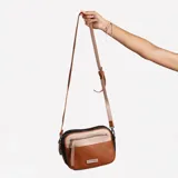 Cartera bandolera de cuero sintético color marrón con detalles en beige y negro. Tiene correa larga regulable, cierre superior y bolsillo frontal con cierre.