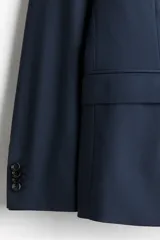 Blazer azul marino de corte slim fit, con solapas de muesca finas, botonadura sencilla de un botón visible, bolsillo superior insertado y dos bolsillos delanteros con solapa. Presenta abertura doble en la espalda y forro interior.