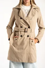Trench impermeable de corte oversize en color camel, con diseño de doble botonadura, solapas clásicas y cinturón ajustable en la cintura.