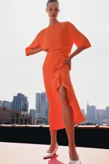 Vestido midi color naranja de la colección ZW de Zara, con cuello redondo, manga corta y detalle de tejido drapeado con volados en el delantero. Cuenta con cierre en la espalda con abertura y botón.