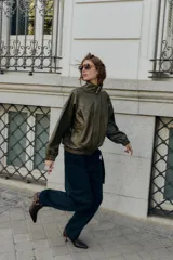 Cazadora estilo bomber color marrón oscuro, con efecto piel, cuello subido y manga larga. Tiene bolsillos delanteros con cierre de cremallera y acabados elásticos en puños y bajo. El cierre frontal es con cremallera y botones a presión ocultos.