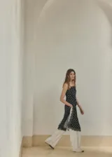 Top largo de tejido satinado color negro con estampado de lunares blancos, diseño recto, tirantes finos y ribetes de encaje negro en el escote y el ruedo.