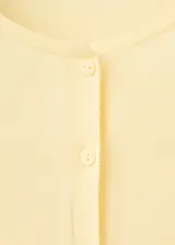 Chaleco de punto fino color amarillo claro, de corte recto, con cuello redondo, manga larga y cierre delantero de botonadura completa.