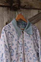 Campera de lona estampada con diseño de caballos y flores, con cuello de pana en color gris azulado y cierre frontal metálico. El interior está forrado en tela de viyela a cuadros.