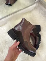 Bota corta de cuero color chocolate con suela track negra. Presenta una combinación de texturas que incluye cuero liso, gamuza y detalles con textura de reptil en la puntera y el talón.