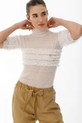 Top de tul semitransparente color blanco, con cuello alto tipo polera, mangas cortas y diseño con frunces y volados horizontales en el pecho y mangas.