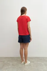 Remera de manga corta color rojo vibrante, con cuello redondo y un panel frontal con bordados calados (ojales) en forma de V invertida.