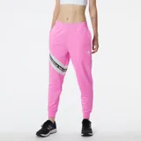 Pantalón de jogging rosa con cintura elástica y cordón ajustable. Presenta una banda lateral blanca con el logo de New Balance repetido.