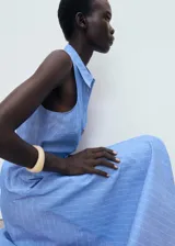 Vestido midi sin mangas confeccionado en mezcla de algodón y lino. Presenta cuello camisero, cierre frontal con botones y cinturón ajustable con hebilla a tono. Diseño de corte evasé con estampado de rayas verticales.