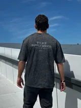 Remera gris con efecto gastado, corte oversize, mangas cortas y estampado en la espalda con el texto "SUPPLY GOODS DESIGNED IN PUNTA DEL ESTE".