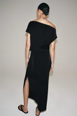 Vestido midi negro confeccionado en hilatura de viscosa, de diseño satinado y corte asimétrico con escote fluido y manga sisa. Presenta bajo acabado en línea evasé y cierre lateral con cremallera oculta en costura.