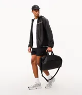 Bolso deportivo cilíndrico de poliéster color negro, con amplio espacio interior, cierre superior con cremallera, asas de mano reforzadas, asa transversal regulable y desmontable, bolsillo frontal con cremallera y bolsillo lateral de malla.