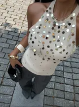 Top blanco de tejido de punto con cuello halter y espalda descubierta. Decorado con apliques de lentejuelas plateadas y doradas.