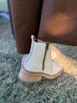 Bota corta de cuero vacuno con textura granulada, color crudo. Presenta cierre lateral metálico, tirador en la parte trasera y suela track de goma en tono contrastante.