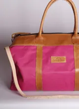 Bolso de lona fucsia combinado con detalles y asas de cuero tostado, de diseño espacioso con cierre superior y correa ajustable.