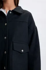 Abrigo corto de paño en color negro, con cuello camisero, cierre frontal con botones metálicos y dos bolsillos delanteros con solapa y botón.