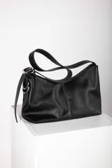 Bandolera de cuero negro de diseño descontracturado, con cierre metálico superior, costuras pespuntadas a contratono y correa ajustable con hebilla metálica y argollas laterales. Cuenta con el logotipo de la marca grabado en la esquina inferior.