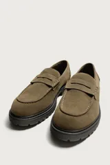 Mocasines de vestir color marrón oscuro, confeccionados en piel con acabado en gamuja serraje. Presentan detalle de antifaz en el empeine con costuras pespunteadas, punta redonda y suela track de goma robusta.