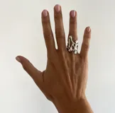 Anillo de diseño orgánico y abstracto con acabado metálico brillante, que presenta una estructura irregular y fluida que envuelve el dedo.