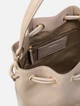 Cartera tipo bucket de Calvin Klein en color beige, confeccionada en poliuretano con asa superior, cierre con cordón ajustable y monograma de la marca grabado en el frente.