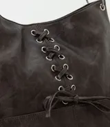 Cartera estilo hobo de cuero sintético color gris oscuro, con diseño de media luna y detalle de cordón cruzado con lazo regulable en el frente. Cuenta con bolsillos frontales funcionales, ojalillos metálicos y correa fija reforzada.