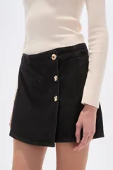 Short pollera de jean color negro, con diseño cruzado frontal y cierre de botones metálicos dorados. Presenta un corte al cuerpo y tiro alto.