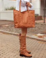 Bota de caña alta confeccionada en cuero color marrón tostado. Presenta un diseño con tres hebillas decorativas en la parte superior de la caña y una correa con hebilla y argolla metálica en el tobillo. Cuenta con suela plana y taco bajo de madera oscura.