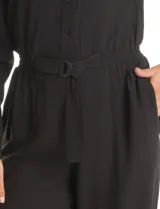 Enterito de crepe negro con cuello camisero, cierre frontal con botones y mangas largas. Presenta cintura elástica con cinto ajustable, bolsillos laterales funcionales y bolsillos simulados en el pecho.