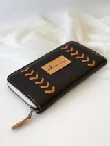 Billetera negra de cuero con cierre metálico, diseño con pespuntes en forma de espiga y logo de la marca en etiqueta de cuero. Incluye monedero interno y espacio para billetes extendidos.