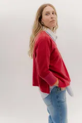 Buzo de punto en color negro con mangas tres cuartos y puños en contraste color marrón. Presenta un diseño holgado con tajos laterales y un aplique circular con logo en la parte inferior.