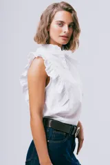 Blusa sin mangas color blanco con cuello alto con volados y detalles de volados en los hombros. Cuenta con cierre frontal de botones.