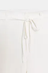 Pantalón blanco de tiro medio con pierna ancha y tejido que contiene lino. Presenta cintura con trabillas y un cinturón ajustable con lazada del mismo tejido. Cierre frontal con cremallera y botón.