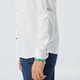 Camisa blanca de lino con cuello mao, manga larga con puños abotonados y bolsillo de parche en el pecho. Cierre frontal con botones a tono.