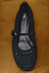 Zapato plano tipo bailarina color negro, con cuerpo trenzado y tira con hebilla en la parte delantera.