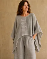 Blusa color vison de corte amplio y asimétrico, con mangas murciélago y detalles de parches rectangulares bordados en el frente.