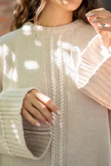 Sweater oversize de tejido de punto color beige, con cuello a la base y mangas largas acampanadas. Presenta detalles bordados a mano en color blanco en el frente, hombros y ruedo.