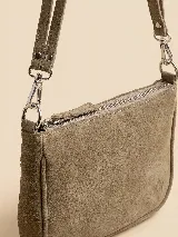 Cartera tipo bandolera de gamuza color verde militar, con cierre superior y herrajes metálicos plateados. Incluye asa corta para llevar al hombro y tiras colgantes decorativas en el lateral.