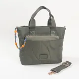 Cartera tipo tote bag color verde oliva, con diseño acolchado de formas circulares y orgánicas. Cuenta con doble asa de mano, bolsillo frontal con cierre y un detalle decorativo de cordón trenzado en colores azul y naranja. Incluye correa larga ajustable y extraíble.