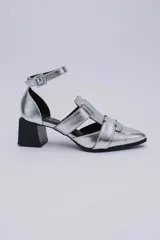 Sandalias plateadas con punta cerrada, tiras entrecruzadas y pulsera al tobillo con hebilla. Taco cuadrado negro.