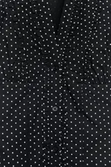 Camisa negra con estampado de lunares blancos, cuello redondo con escote en pico, mangas cortas abullonadas y detalle de volantes frontales. Cierre frontal con botones.