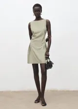 Vestido corto de diseño recto y sin mangas, con cuello barco y detalle de pliegues laterales en la falda. Cuenta con cierre de cremallera en la parte posterior y forro interior.