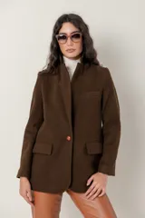 Blazer de paño de lana color marrón chocolate, con cuello mao y un solo botón frontal. Presenta un bolsillo superior de ojal y dos bolsillos de parche inferiores.
