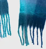 Bufanda amplia tipo mantón con diseño de cuadros en tonos azules y celestes, con flecos en los extremos.