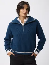 Sweater de tejido grueso en color beige, con cuello alto y cierre frontal parcial. Presenta detalles de rayas negras en contraste en el borde del cuello y en los puños.