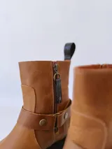 Bota de cuero color marrón con suela de goma negra, cierre lateral y pulsera desmontable con hebilla.