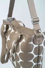 Bolso tipo tote con estampado de círculos blancos sobre fondo beige, doble asa corta y correa larga desmontable.
